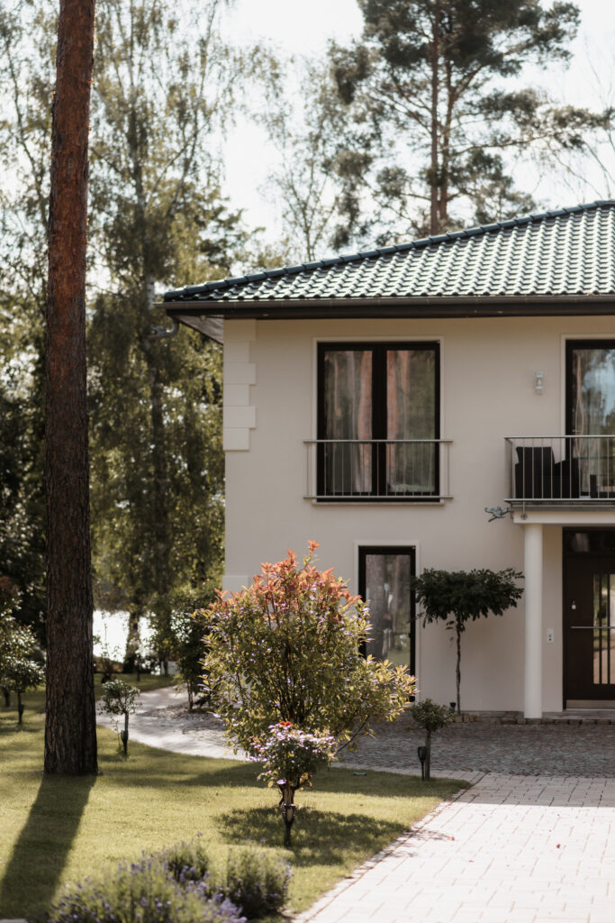 Modernes zweistöckiges Haus mit großen Fenstern, einem begrünten Dach und Bäumen in einem begrünten Hof - ein ideales Berliner Domizil für eine stilvolle Hochzeitsdeko oder Familienfeiern.