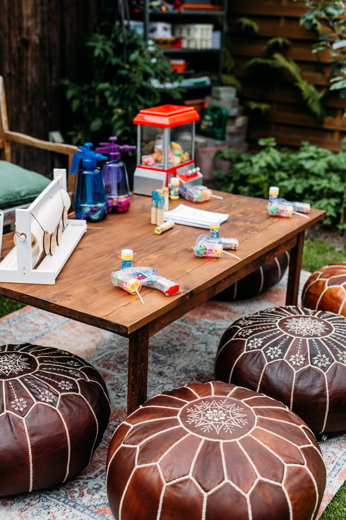 Ein niedriger Holztisch mit Partygeschenken, Karnevalsspielzeug und runden Lederhockern im Freien - perfekt für eine Berliner oder Brandenburger Veranstaltung, die von einem erfahrenen Hochzeitsplaner gestaltet wird.
