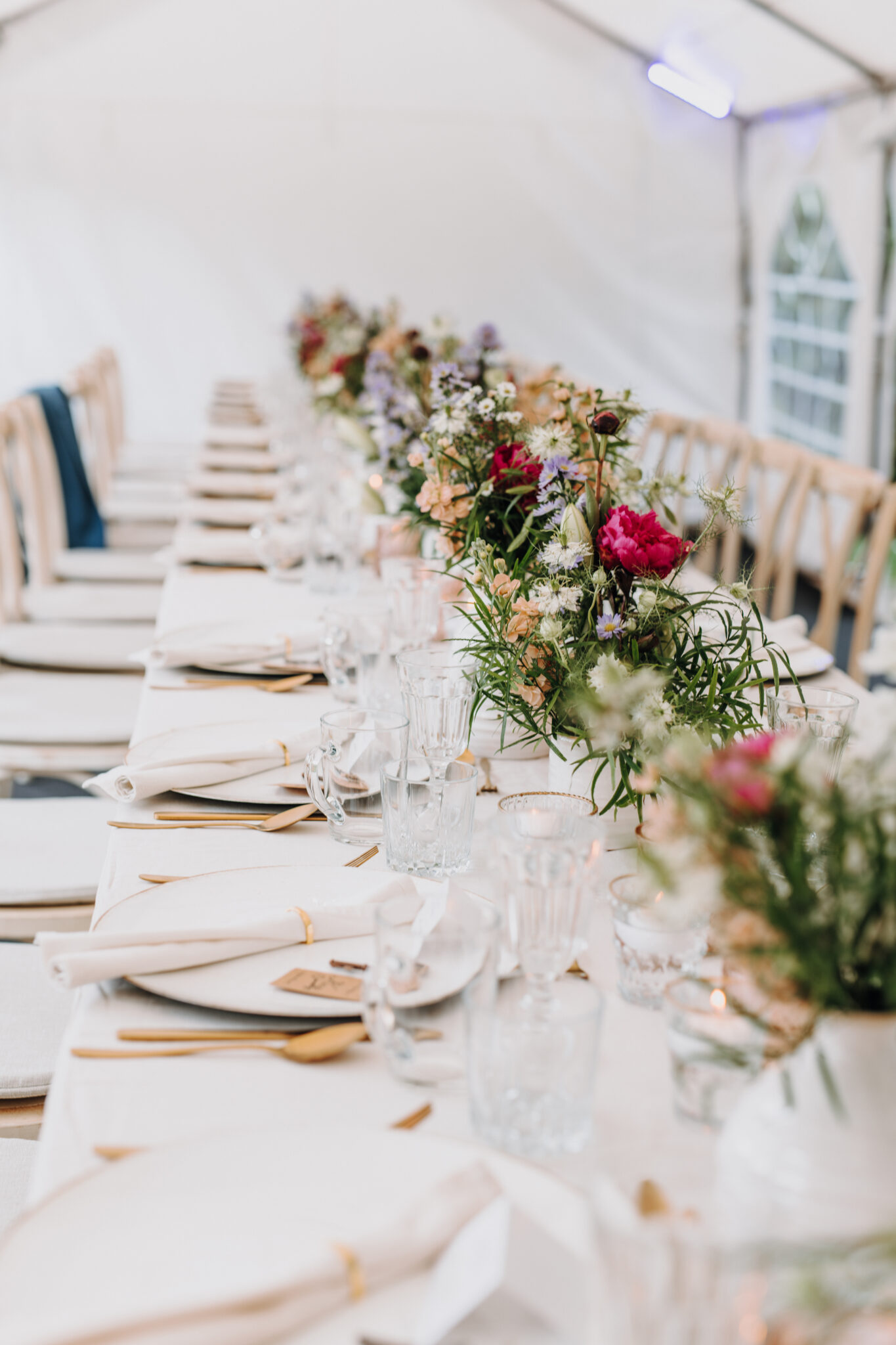 Ein langer Esstisch mit weißer Bettwäsche, Gläsern und Blumenschmuck in einem hellen, luftigen Zelt in der Nähe von Berlin - perfekt für eine brandenburgische Feier oder eine Zeremonie, die von einer Freien Traurednerin geleitet wird.