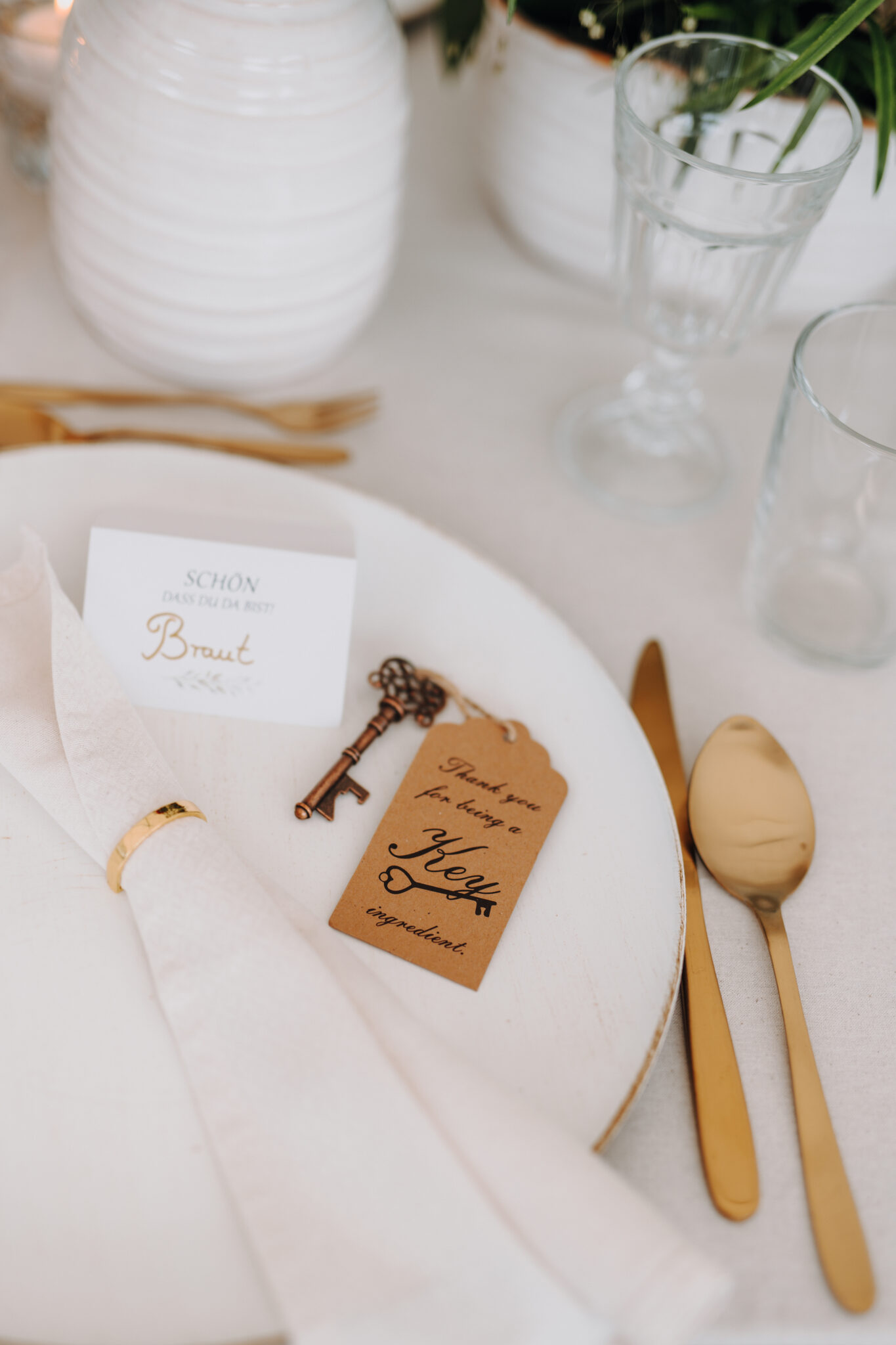 Elegante Tischdekoration mit goldenem Besteck, Serviette, Namenskarte und einem Vintage-Schlüssel an einem dekorativen Anhänger - die perfekte Hochzeitsdeko für Hochzeiten in Brandenburg oder eine Inspiration von einem professionellen Hochzeitsplaner.
