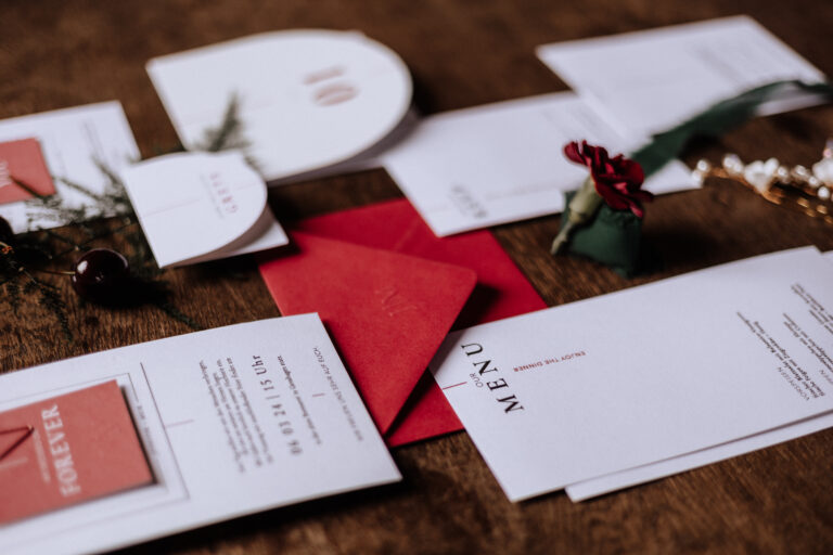 Hochzeitspapeterie, einschließlich Menüs, Einladungen und Umschläge, arrangiert auf einer hölzernen Oberfläche mit floralen Akzenten - perfekt für Feiern in Berlin oder Brandenburg und mit einer Freien Traurednerin im Hinterkopf gestylt.