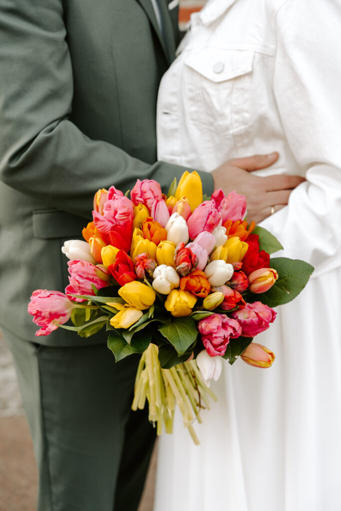Eine Person in Weiß hält einen bunten Tulpenstrauß und steht neben einer Person in einem grünen Anzug - vielleicht nach einer Zeremonie, die von einer Freien Traurednerin in Berlin geleitet wird.