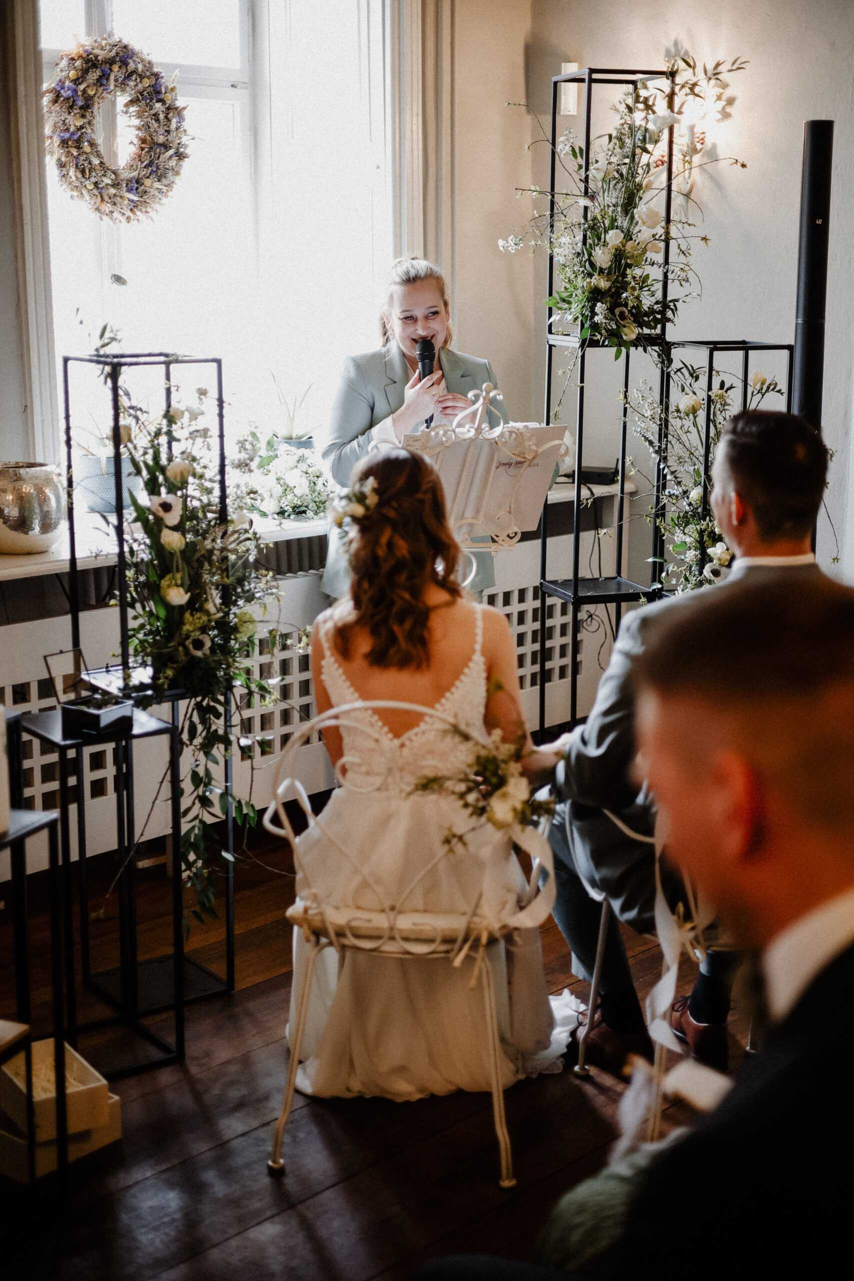 Braut und Bräutigam sitzen bei einer wunderschön dekorierten Indoor-Hochzeitszeremonie mit eleganter Hochzeitsdeko, die von einem erfahrenen Hochzeitsplaner aus Brandenburg arrangiert wurde, dem Trauredner gegenüber.