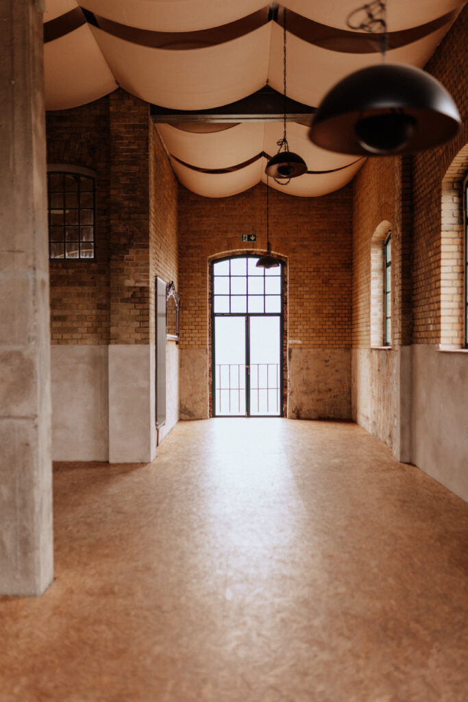 Sonnenlicht fällt durch eine Glastür und erhellt den leeren Flur mit Backsteinwänden und Bogenfenstern in Berlin - ein perfekter Ort für alle Hochzeitsplaner und Freien Trauredner, die zeitlosen Charme suchen.
