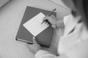 Eine Person schreibt auf eine leere Karte, die oben auf ein geschlossenes Buch gelegt wird - vielleicht schreibt sie ein Eheversprechen für eine Freie Traurednerin in Berlin oder Brandenburg.
