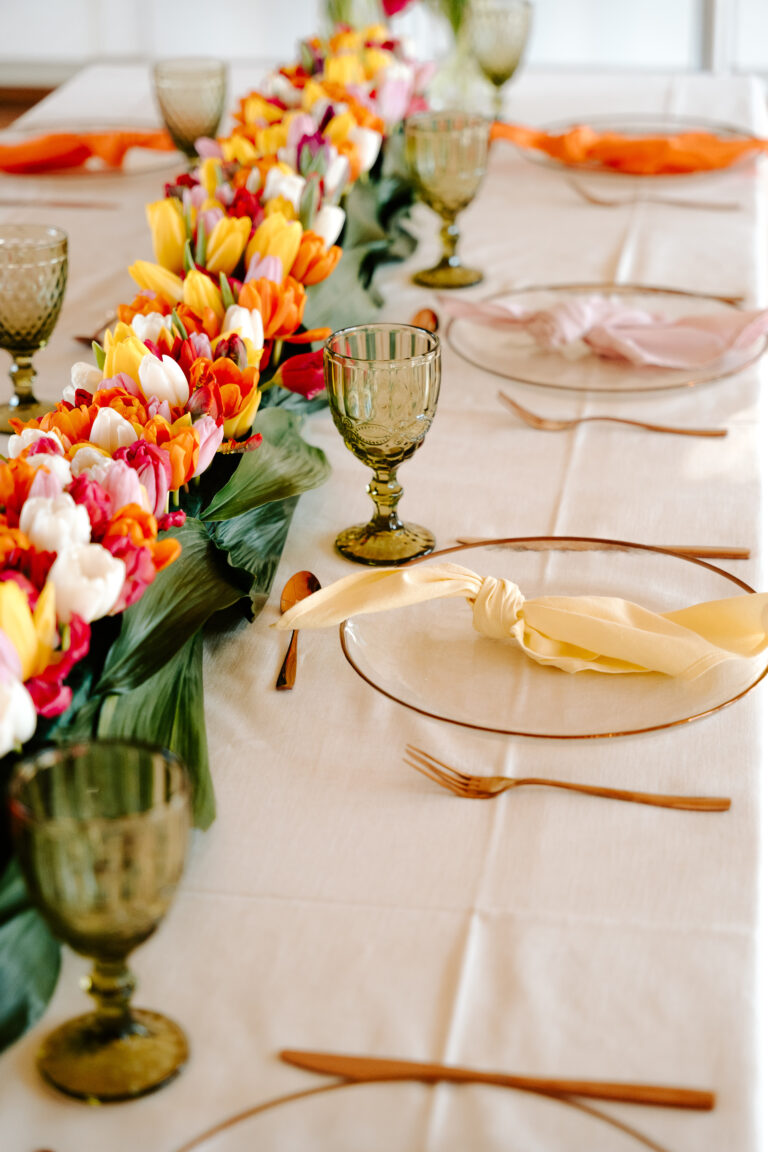 Ein gedeckter Tisch mit grünen Gläsern, goldenen Utensilien und einem bunten Blumenläufer - die perfekte Hochzeitsdeko für Ihre Feier in Brandenburg, kuratiert von einer erfahrenen Freien Traurednerin.