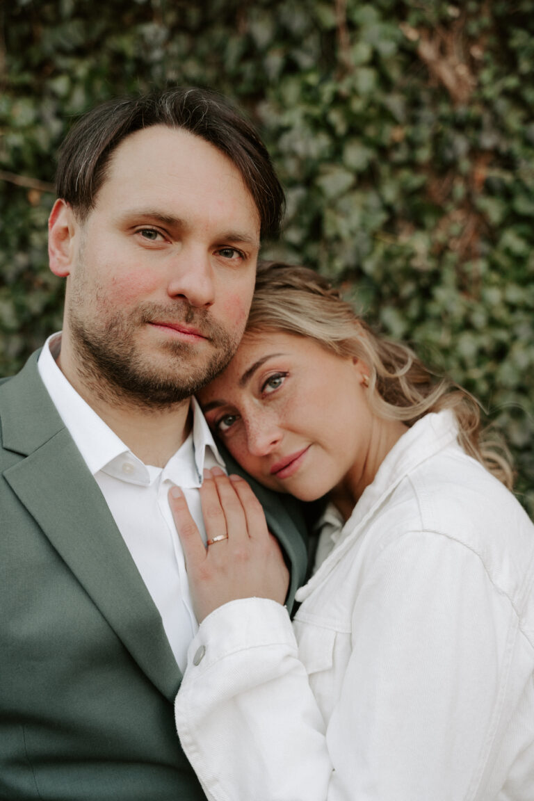 Eine Frau lehnt sich an die Schulter eines Mannes und zeigt einen Verlobungsring, beide stehen vor einer grünen Kulisse - die perfekte Inspiration für Hochzeitsplaner oder eine Freie Traurednerin in Brandenburg.