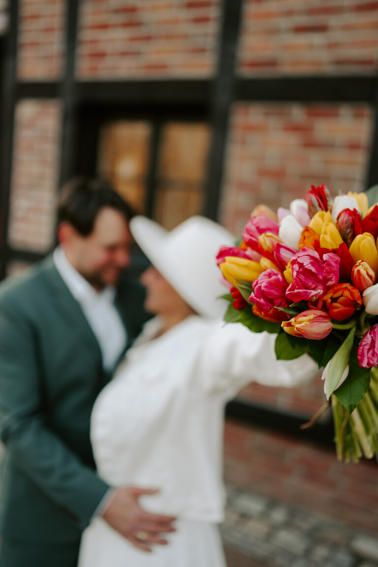 Ein Paar umarmt sich, während es einen bunten Tulpenstrauß im Vordergrund hält, aufgenommen während einer herzlichen Zeremonie mit einer Freien Traurednerin in Brandenburg.