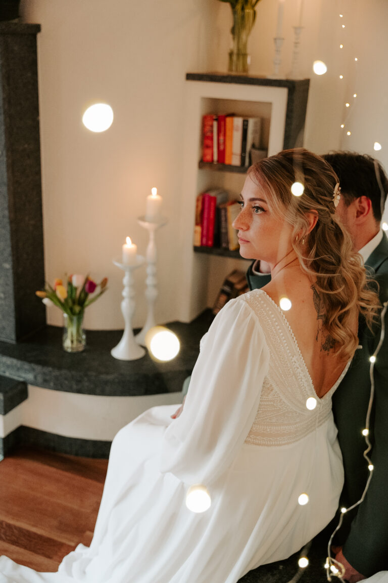 Die Braut im weißen Kleid sitzt mit ihrem Bräutigam bei Kerzen und Blumen, beleuchtet von Lichterketten im Vordergrund - ein romantischer Moment, den jeder Hochzeitsplaner in Brandenburg oder die Freie Traurednerin perfekt in Szene setzen kann.