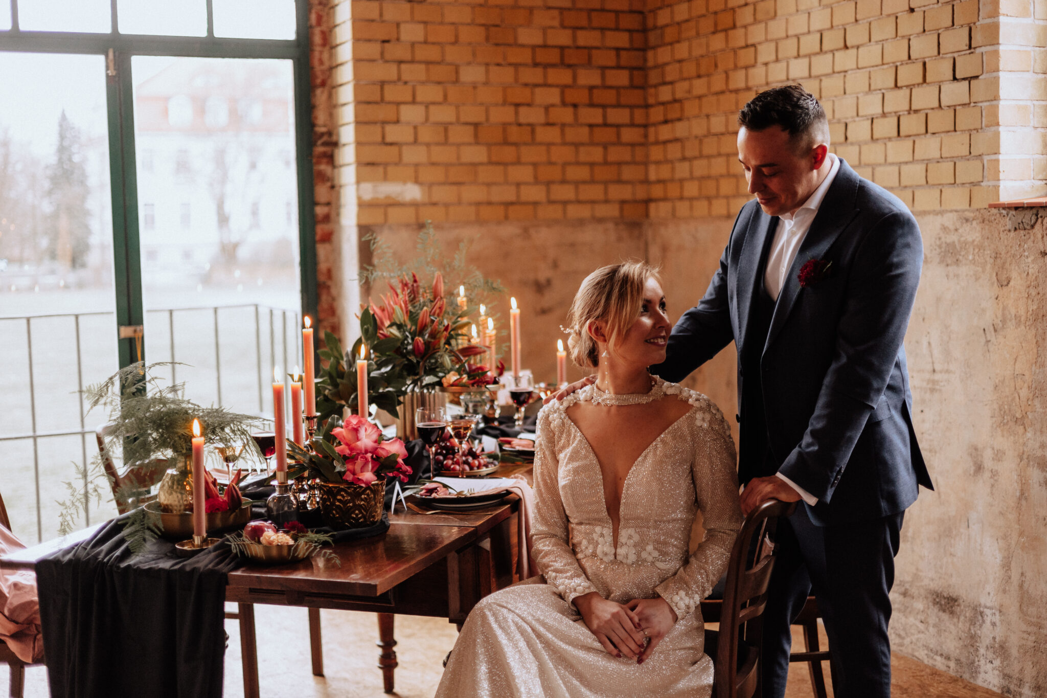 Eine Braut sitzt an einem geschmückten Tisch in Brandenburg, während der Bräutigam neben ihr steht und sie sanft an der Schulter berührt - ein magischer Moment, der durch einen erfahrenen Hochzeitsplaner und eine einfühlsame Freie Traurednerin zum Leben erweckt wird.