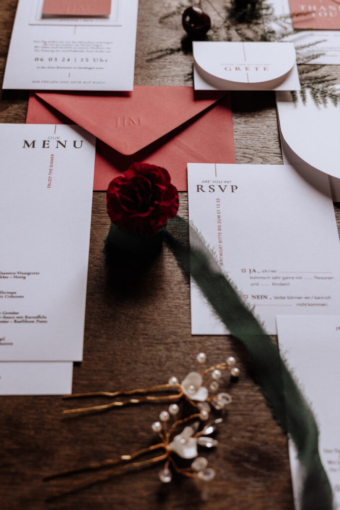 Elegante Hochzeitspapeterie mit RSVP, Menü und roter Rose auf einem Holztisch, verziert mit grünem Band - perfekt für Paare in Berlin oder Brandenburg, die sich von einem lokalen Hochzeitsplaner inspirieren lassen möchten.