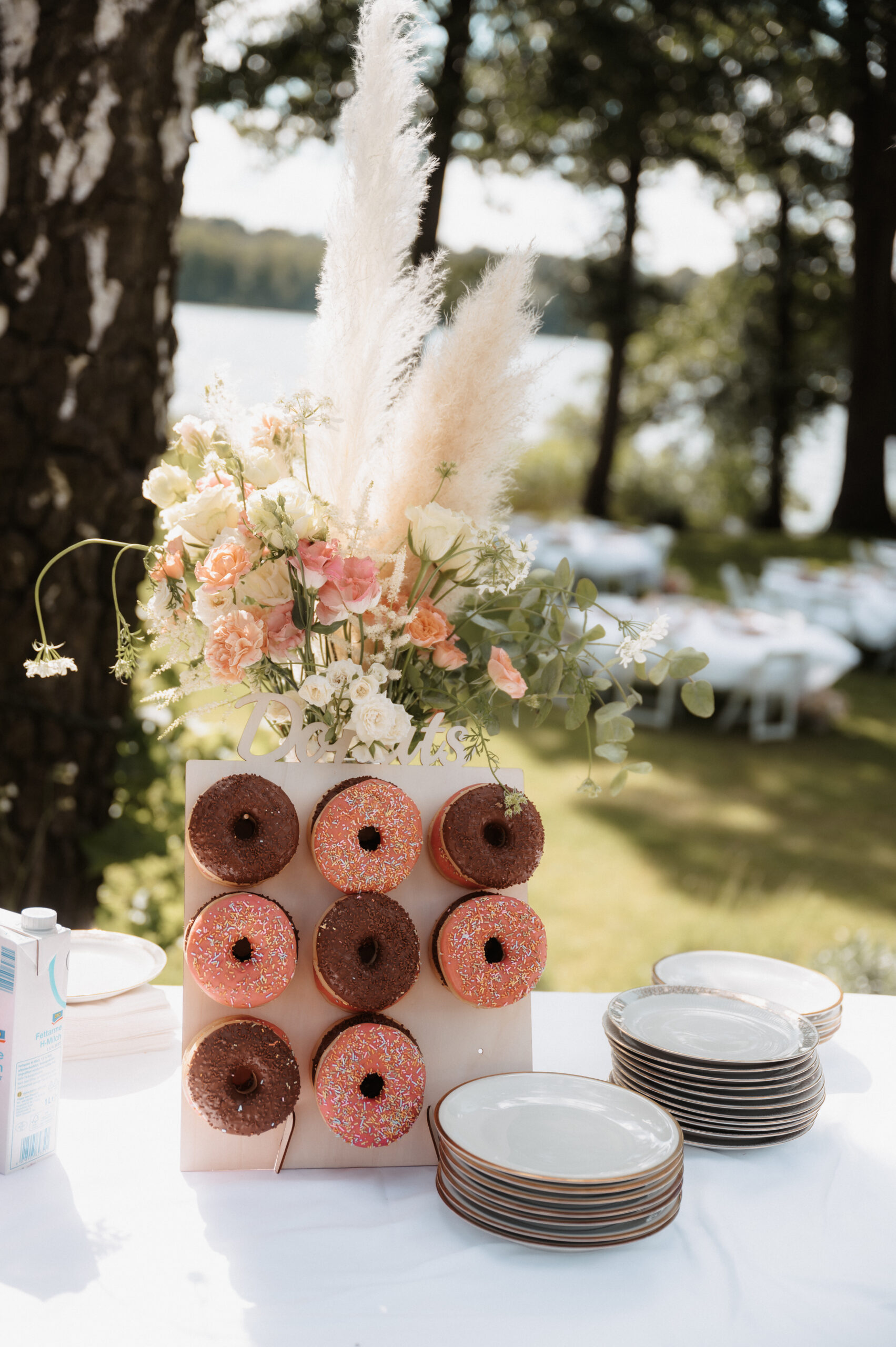 Eine Donut-Wand mit Blumen, Tellern und gestapelten Donuts auf einem Tisch im Freien bei einer Gartenveranstaltung - die perfekte Hochzeitsdeko-Inspiration für Feiern in Berlin, vor allem, wenn eine Freie Traurednerin Ihre Zeremonie leitet.