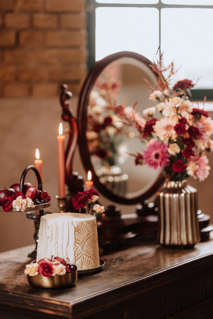 Eine dekorierte Torte, Blumen und Kerzen stehen auf einem Holztisch vor einem alten Spiegel - die perfekte Inspiration für jeden Hochzeitsplaner in Brandenburg.