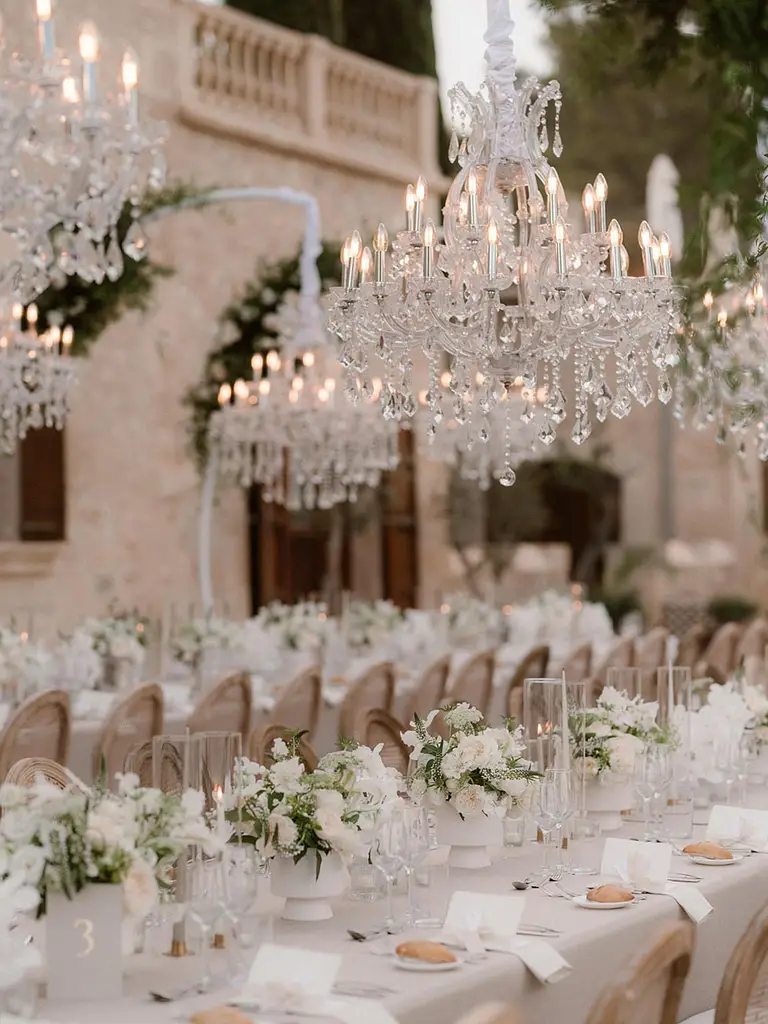 Elegante Hochzeitstafel im Freien mit weißen Blumen, Kristalllüstern und ordentlich gedeckten Tischen - perfekt für eine mediterrane Hochzeit oder Freie Trauung auf Mallorca, um einen unvergesslichen Hochzeitstraum zu schaffen.