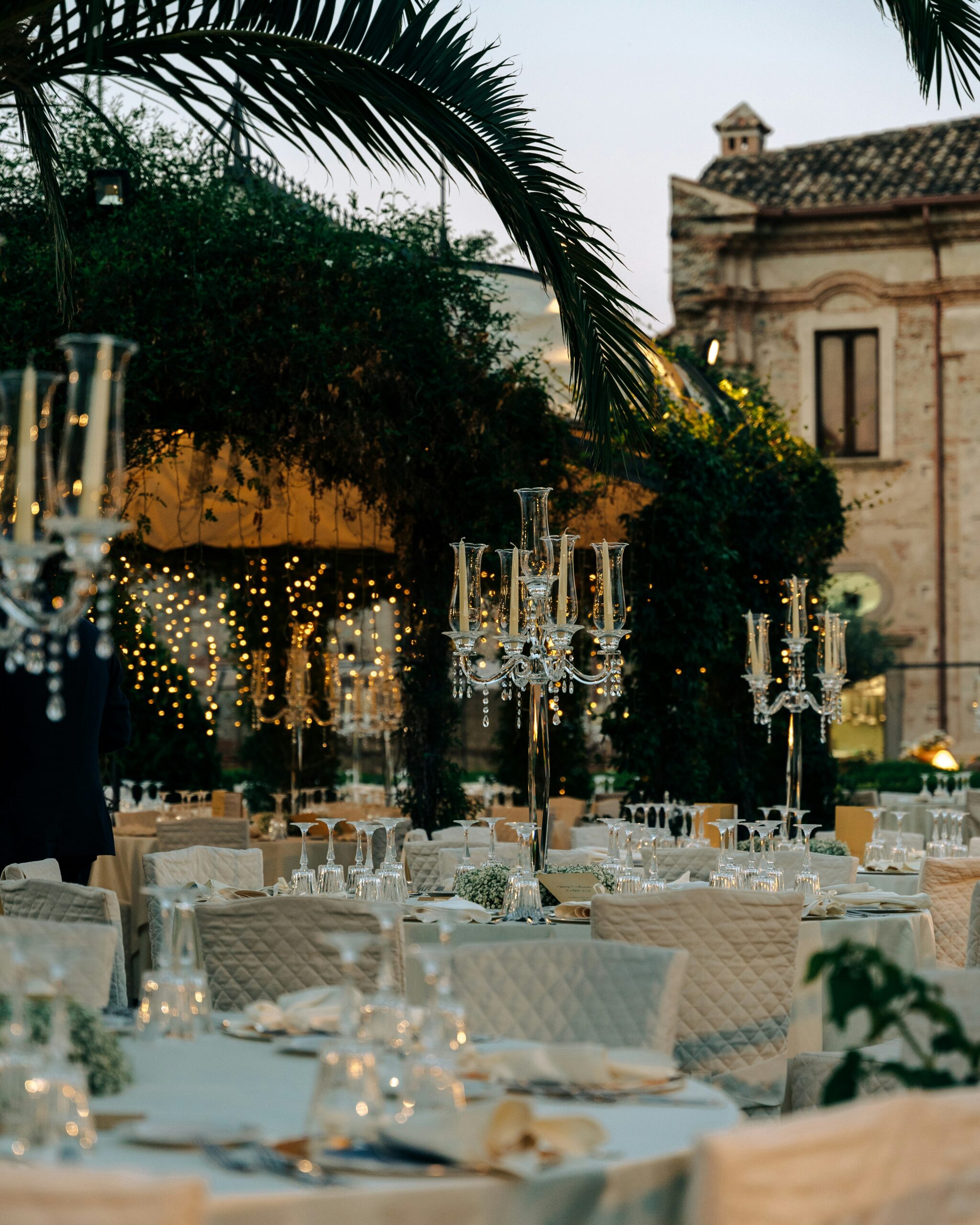 Elegante Hochzeitsfeier im Freien mit runden Tischen, Kristallkandelabern und Lichterketten unter Palmen - perfekt für einen mediterranen Hochzeitstraum oder eine unvergessliche Freie Trauung Mallorca.