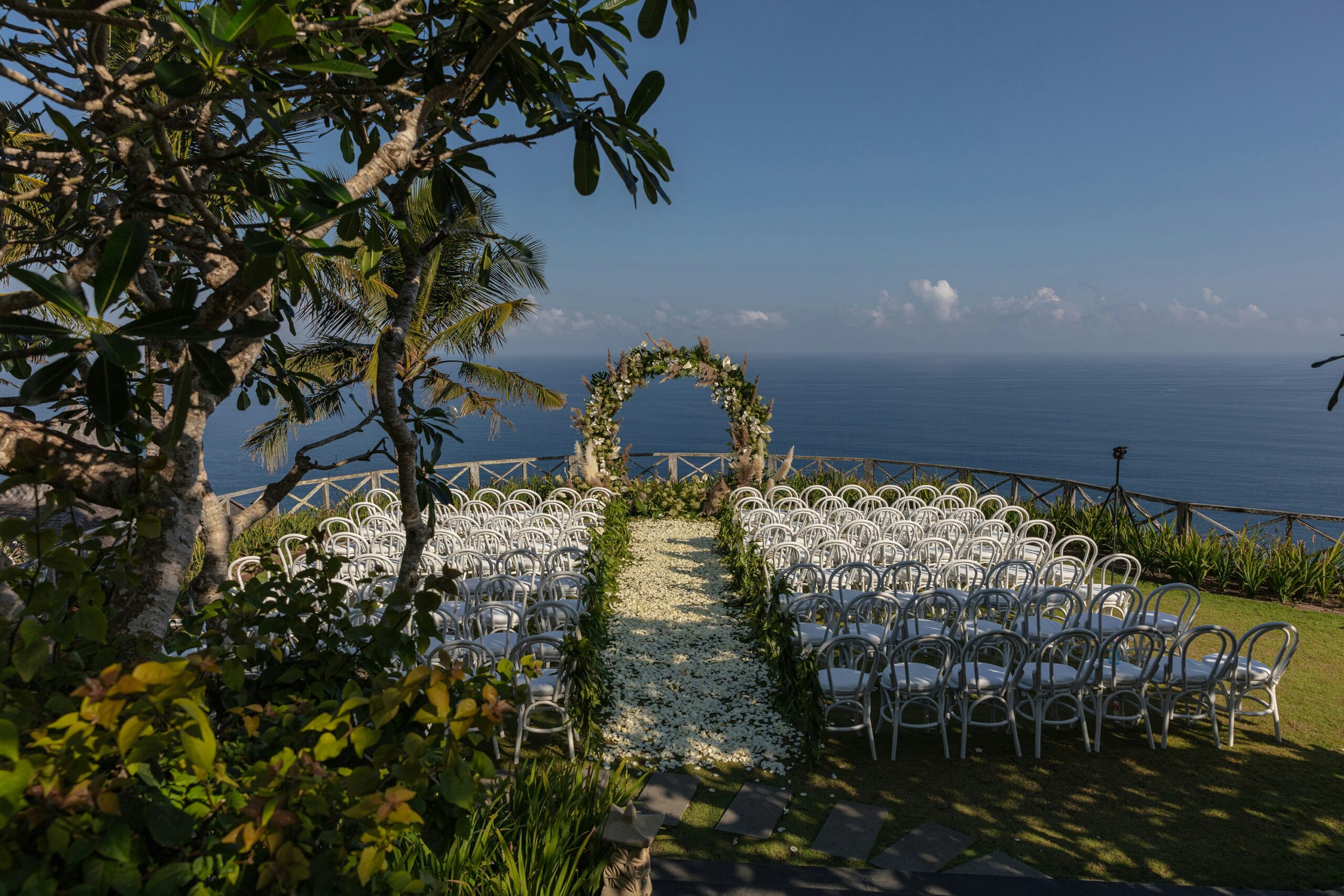 Hochzeit im Freien mit weißen Stühlen und einem Blumenbogen mit Blick auf das Meer unter einem klaren blauen Himmel - ein wahrer mediterraner Hochzeitstraum für eine unvergessliche Freie Trauung auf Mallorca.