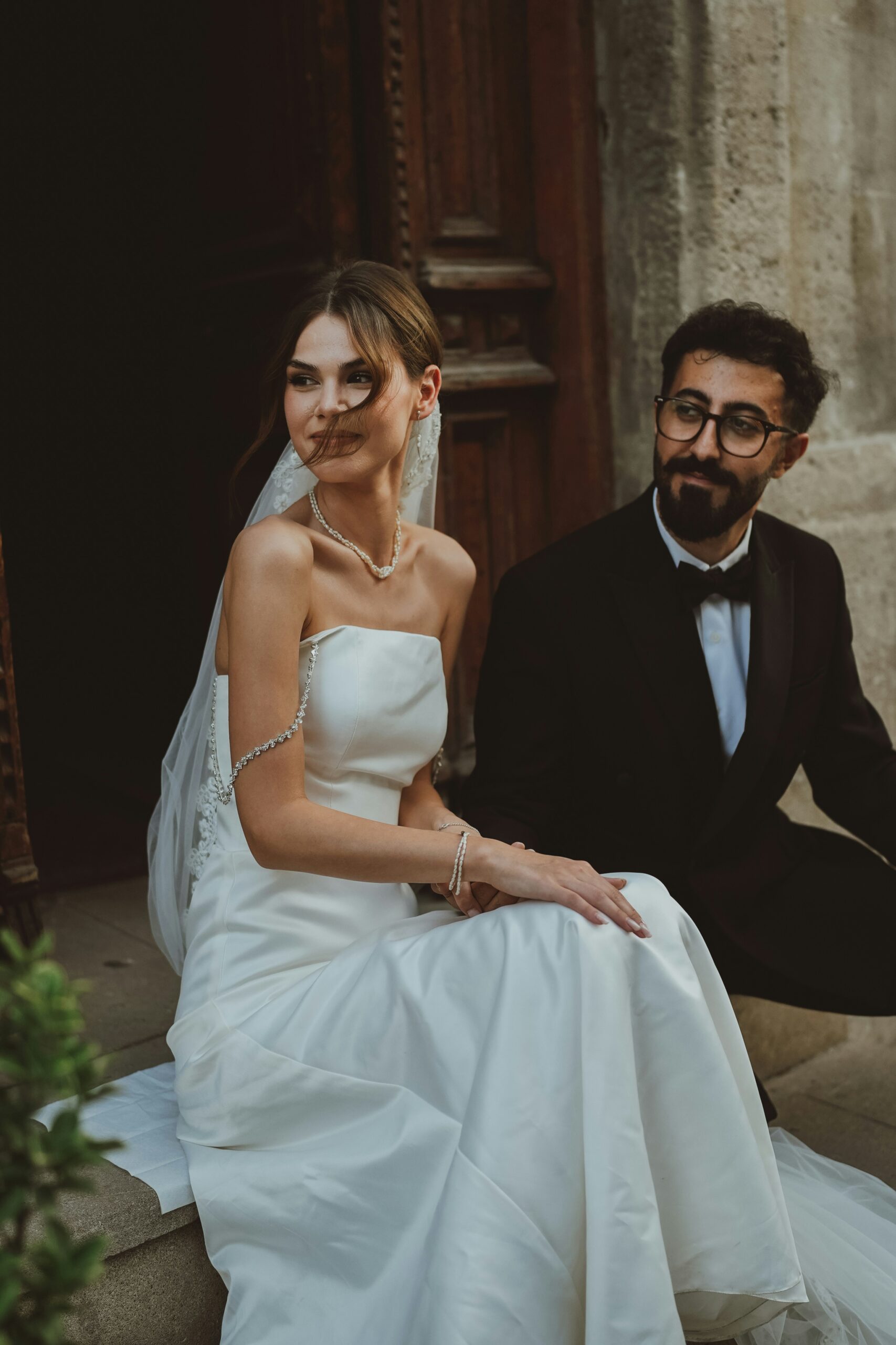 Eine Braut in einem weißen Kleid und ein Bräutigam im Smoking sitzen zusammen auf Steinstufen und fangen die Essenz eines mediterranen Hochzeitstraums während ihrer Freien Trauung auf Mallorca ein.