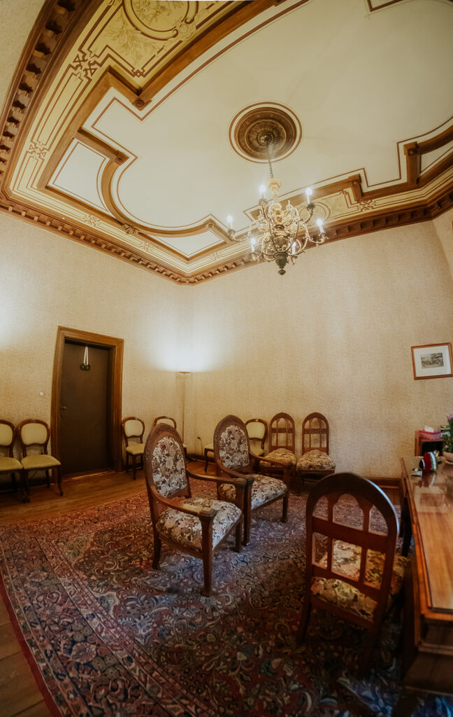 Verschnörkelter Vintage-Raum mit gemusterten Stühlen, Kronleuchter, dekorativer Decke und einem großen Teppich - perfekt für eine Freie Trauung oder eine intime Standesamt-Zeremonie.