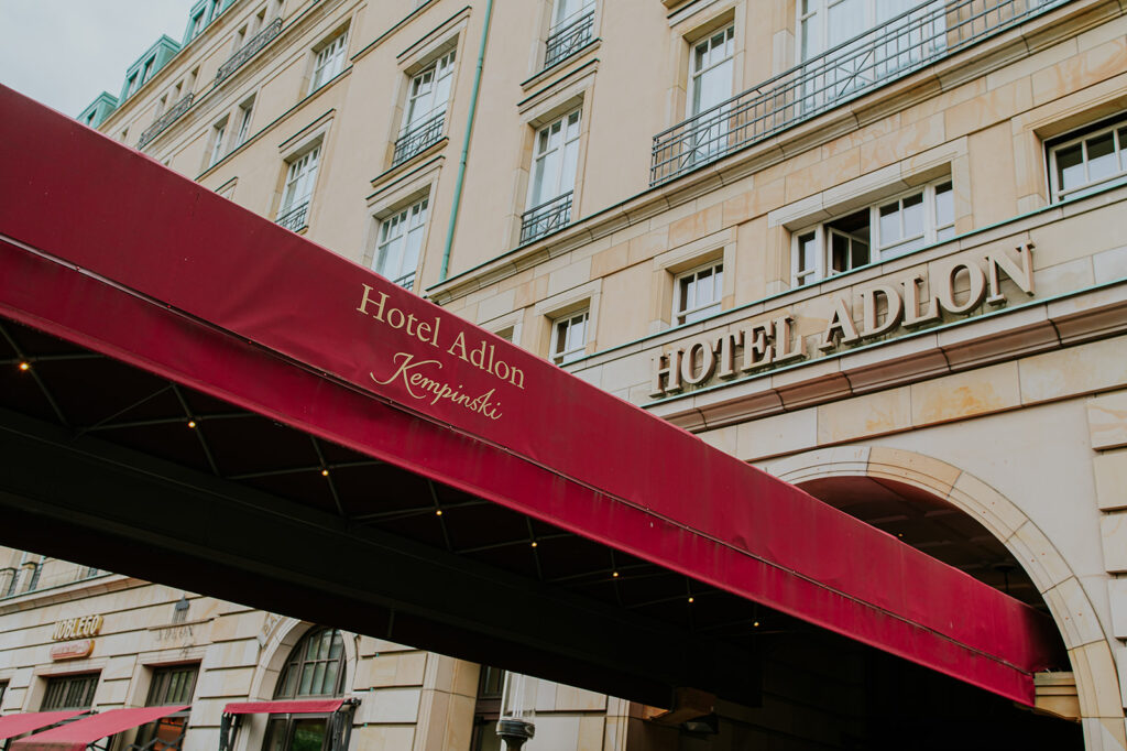 Rote Markise mit dem Schriftzug Hotel Adlon Berlin vor der großen beigen Fassade des Hotel Adlon Kempinski.