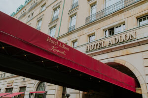 Rote Markise mit dem Schriftzug Hotel Adlon Berlin vor der großen beigen Fassade des Hotel Adlon Kempinski.
