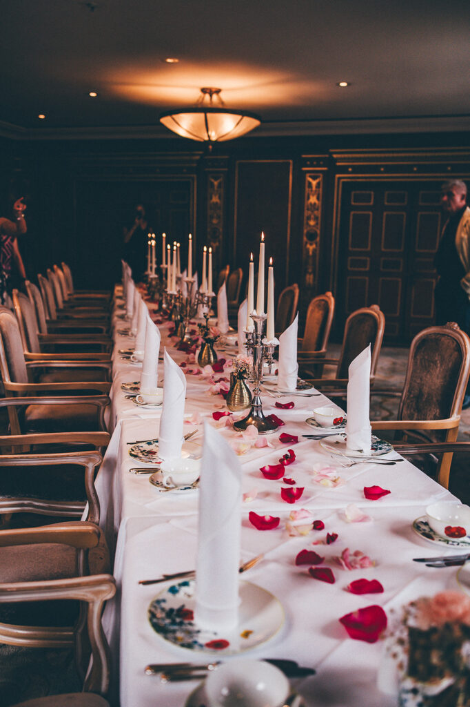 Ein langer, eleganter Banketttisch, gedeckt mit weißen Servietten, Kerzen und Rosenblättern in einem formellen Speisesaal - perfekt für eine Signature Wedding Berlin Feier.