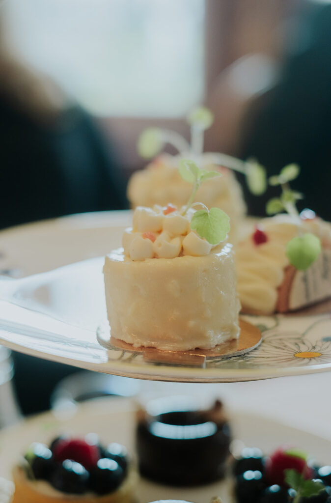 Eine kleine, elegante weiße Torte mit cremigem Zuckerguss und Microgreens auf einem dekorativen Teller, der an die raffinierten Desserts des Hotel Adlon Berlin erinnert.