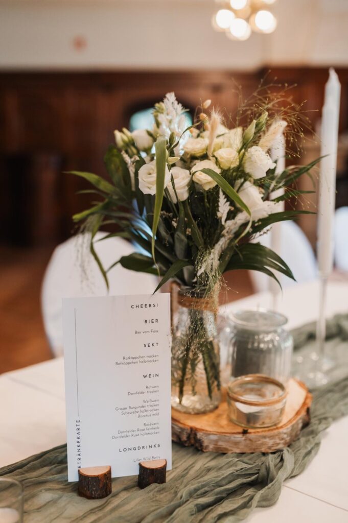 Ein floraler Tafelaufsatz mit einer Menükarte auf einem dekorierten Tisch für eine Veranstaltung oder einen Empfang, perfekt für die Hochzeitsdeko in Berlin und erhältlich bei Dekoverleih services.