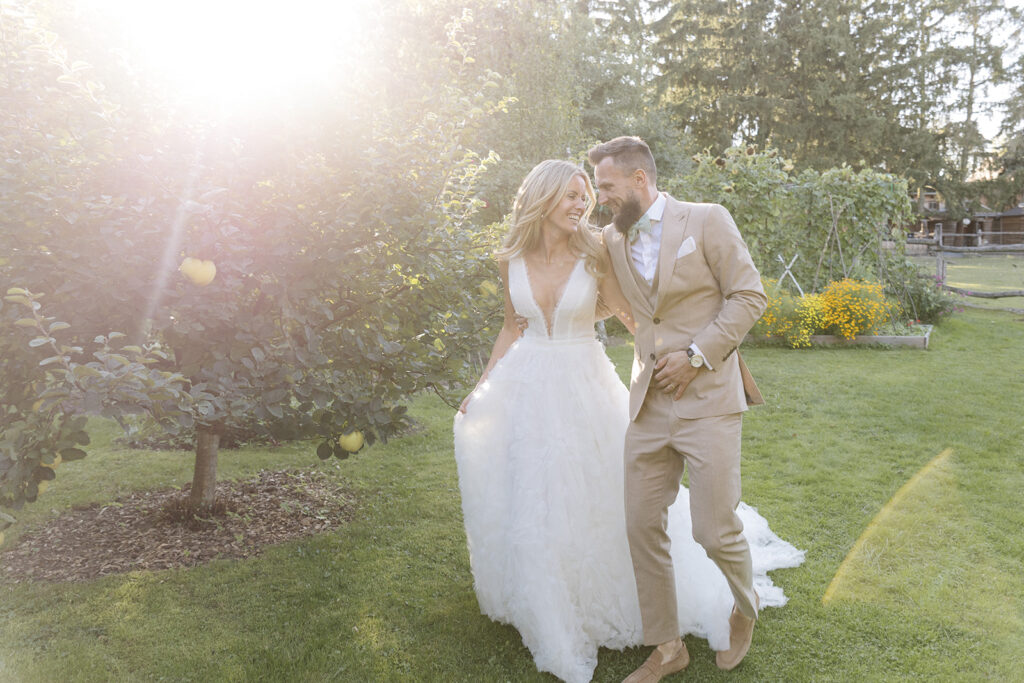 N&M, das fröhliche Brautpaar, lacht gemeinsam, während es nach der Freien Trauung durch einen sonnigen Garten spaziert.