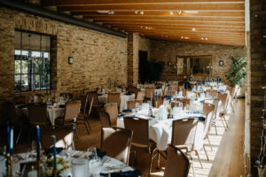 Sonnendurchfluteter Bankettsaal mit runden Tischen, die für eine Veranstaltung gedeckt sind, umgeben von braunen Stühlen und freiliegenden Backsteinwänden.