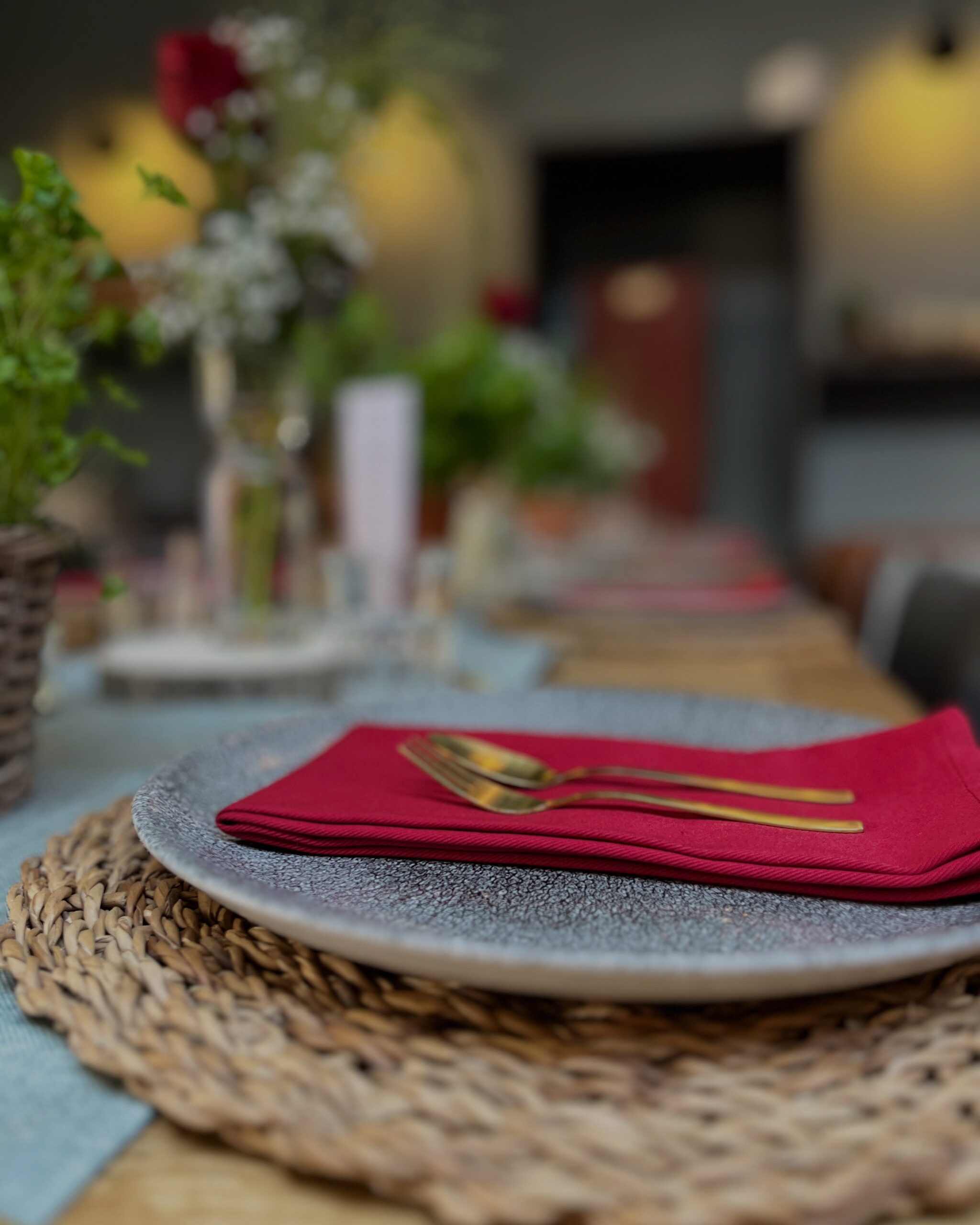 Eine Nahaufnahme eines gedeckten Tisches von Dekorationsservice Daniela mit einer roten Serviette und goldenem Besteck auf einem Teller, mit einem schön verschwommenen Hintergrund.