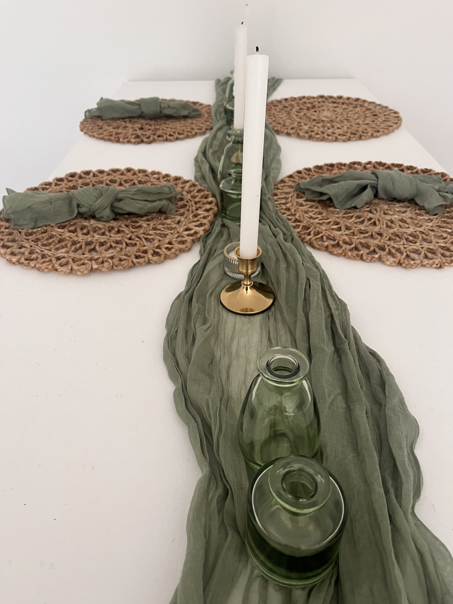 Gedeckter Tisch mit gewebten Tischsets, grünen Servietten, grünen Vasen, weißen Kerzen und einem grünen Tischläufer.